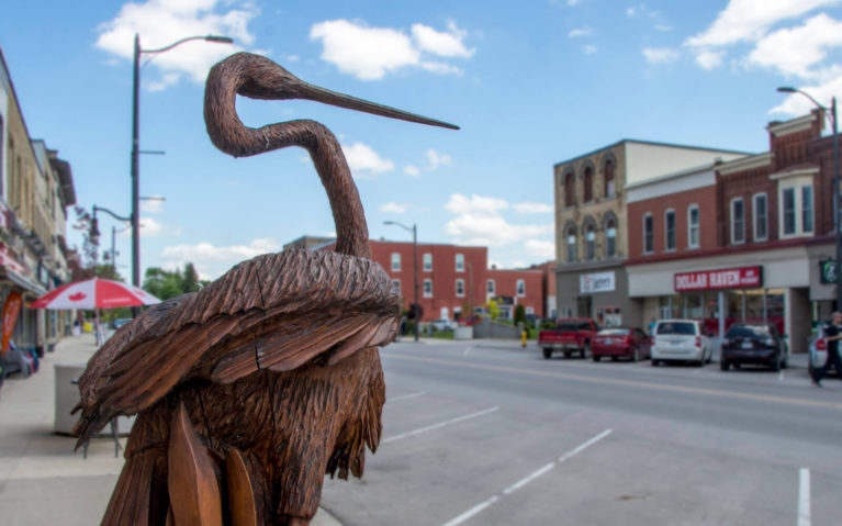 View of the Main Street in the Town of Mitchell, Focusing on a Heron Statue Carved from Wood :: I've Been Bit! Travel Blog